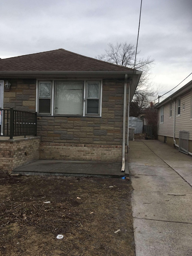 view of side of home featuring stone siding and roof with shingles