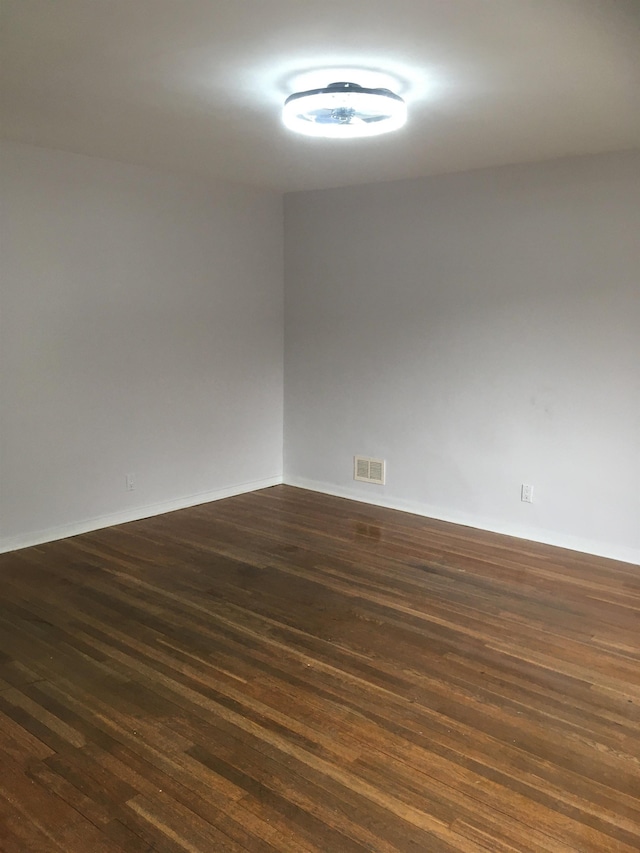 empty room with dark wood-style floors, baseboards, and visible vents