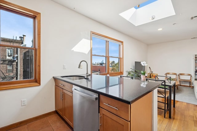 kitchen with a peninsula, baseboards, a sink, dishwasher, and a skylight