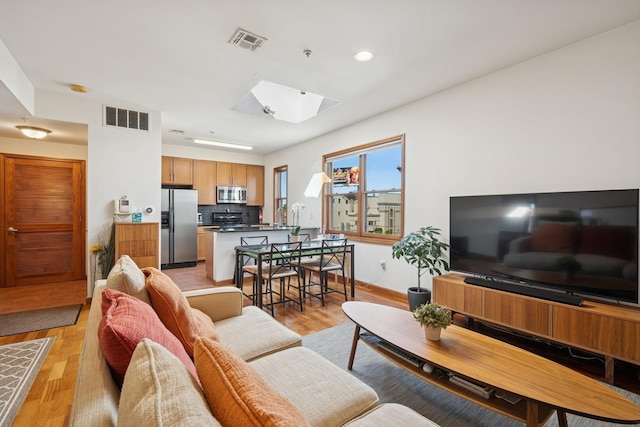 living room featuring a skylight, recessed lighting, light wood finished floors, and visible vents