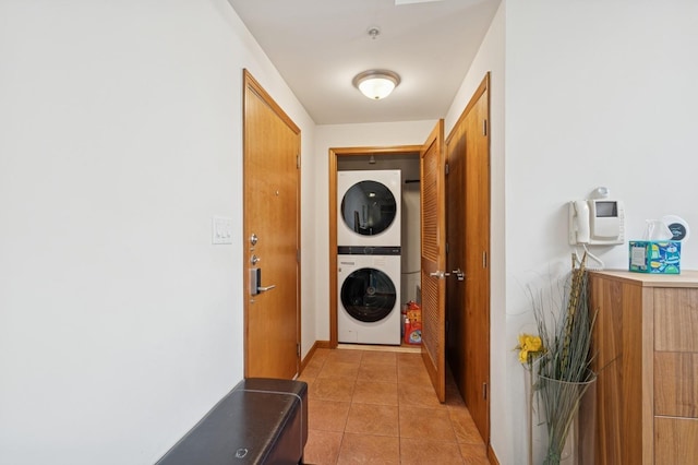 laundry area with baseboards, laundry area, light tile patterned floors, and stacked washer and clothes dryer