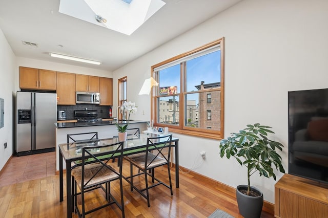 dining area with a skylight, baseboards, light wood-type flooring, and visible vents