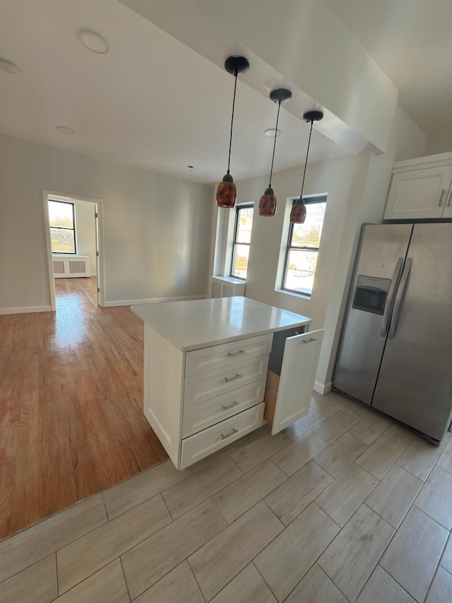 kitchen with radiator heating unit, decorative light fixtures, white cabinets, stainless steel fridge with ice dispenser, and a center island