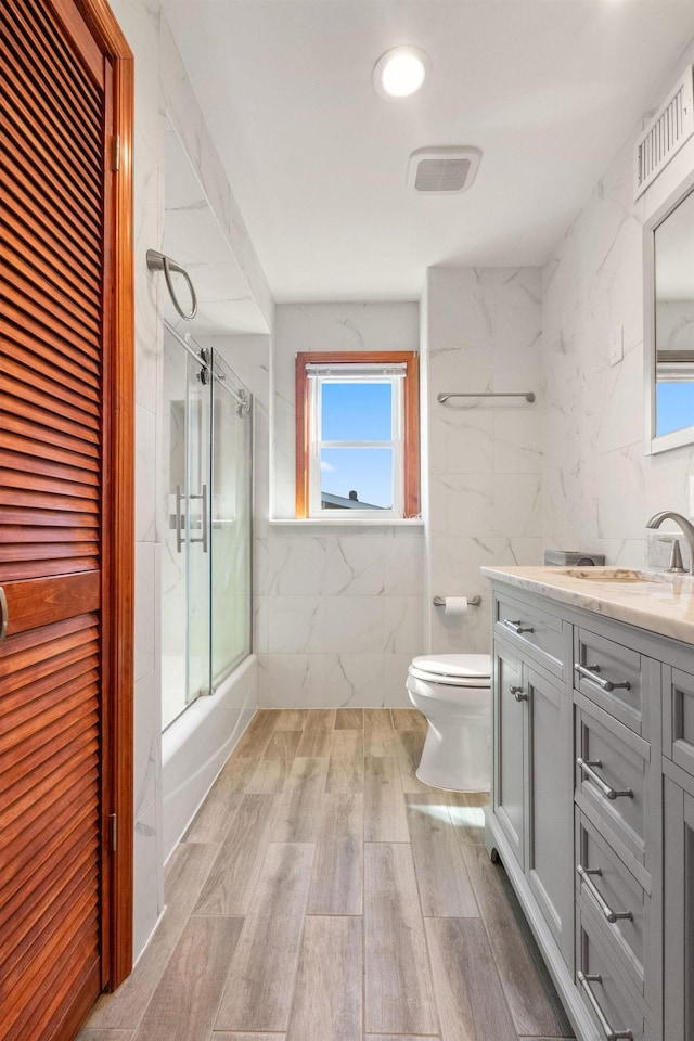 22 W 34th St Unit G, Bayonne, NJ 07002 - full bath featuring toilet, vanity, wood finished floors, shower / bath combination with glass door, and tile walls