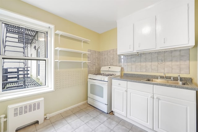 kitchen featuring radiator heating unit, white range with gas cooktop, a sink, white cabinets, and backsplash