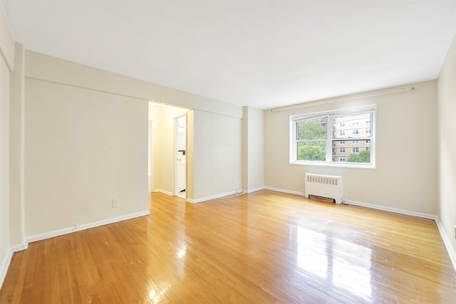 spare room with radiator heating unit, light wood-style flooring, and baseboards