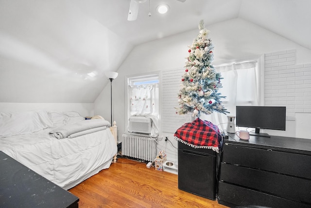 bedroom with lofted ceiling, radiator heating unit, cooling unit, and wood finished floors