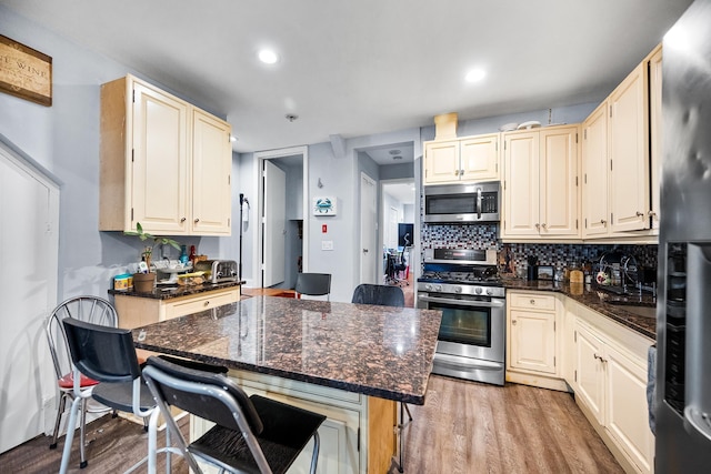 kitchen with tasteful backsplash, appliances with stainless steel finishes, light wood-style floors, dark stone countertops, and a kitchen bar