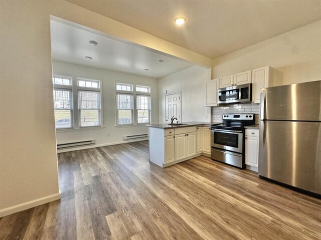 549 Pavonia Ave Unit 1 & 2, Jersey City, NJ 07306 - kitchen featuring appliances with stainless steel finishes, a peninsula, baseboard heating, light wood-style flooring, and decorative backsplash