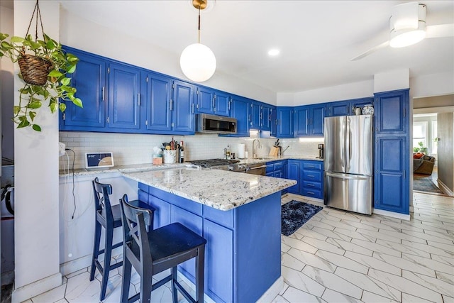 kitchen featuring a peninsula, blue cabinetry, a sink, stainless steel appliances, and tasteful backsplash