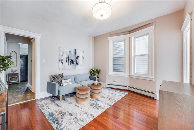 living area featuring a baseboard heating unit, baseboards, and wood finished floors