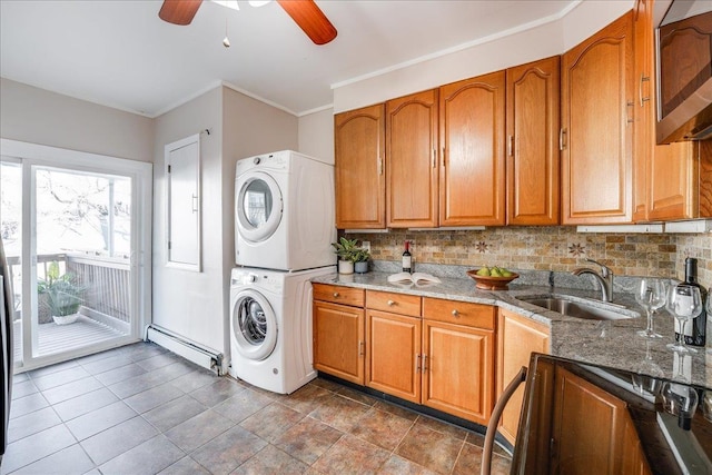 clothes washing area featuring stacked washer and clothes dryer, ornamental molding, a sink, a baseboard heating unit, and laundry area