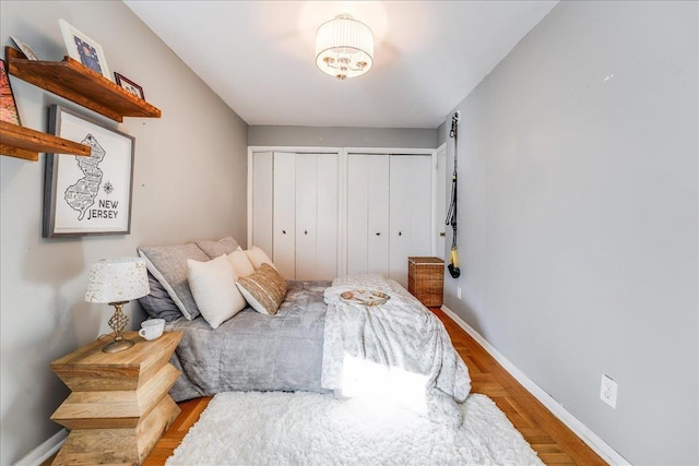 bedroom with wood finished floors, baseboards, and two closets