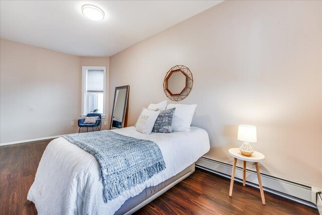 bedroom featuring a baseboard heating unit, baseboards, and wood finished floors