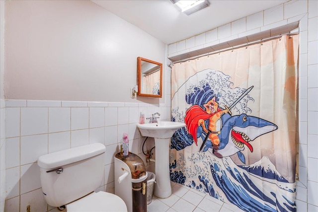 full bathroom featuring toilet, wainscoting, a shower with curtain, tile patterned floors, and tile walls