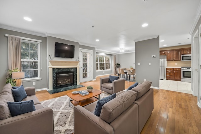 living room with light wood-type flooring, a premium fireplace, baseboards, and crown molding