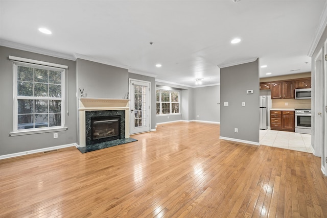 unfurnished living room featuring ornamental molding, recessed lighting, light wood finished floors, a premium fireplace, and baseboards