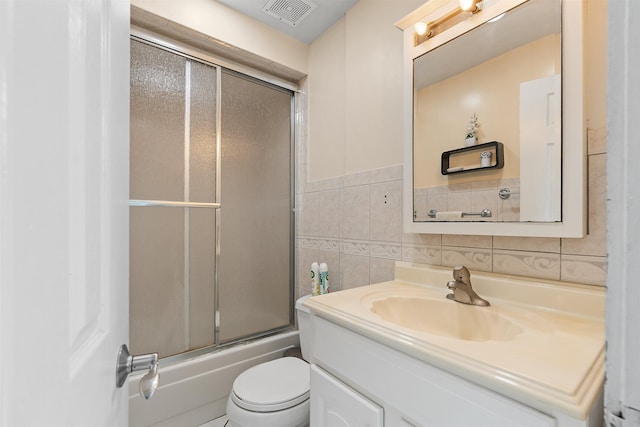 bathroom featuring toilet, shower / bath combination with glass door, vanity, visible vents, and tile walls