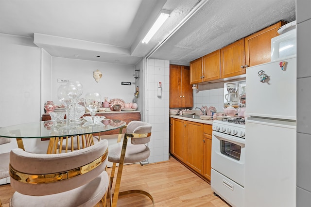 kitchen featuring brown cabinets, tasteful backsplash, light countertops, light wood-type flooring, and white appliances