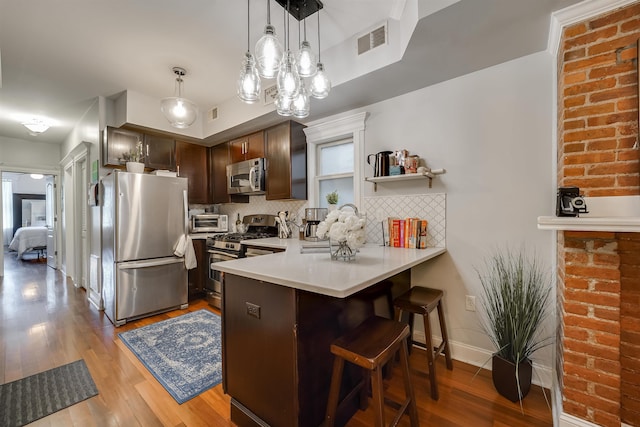 380 7th St Unit 2A, Jersey City, NJ 07302 - kitchen with appliances with stainless steel finishes, a peninsula, a kitchen bar, decorative backsplash, and wood finished floors