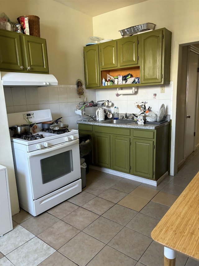 kitchen with under cabinet range hood, a sink, green cabinetry, white gas range, and light tile patterned floors