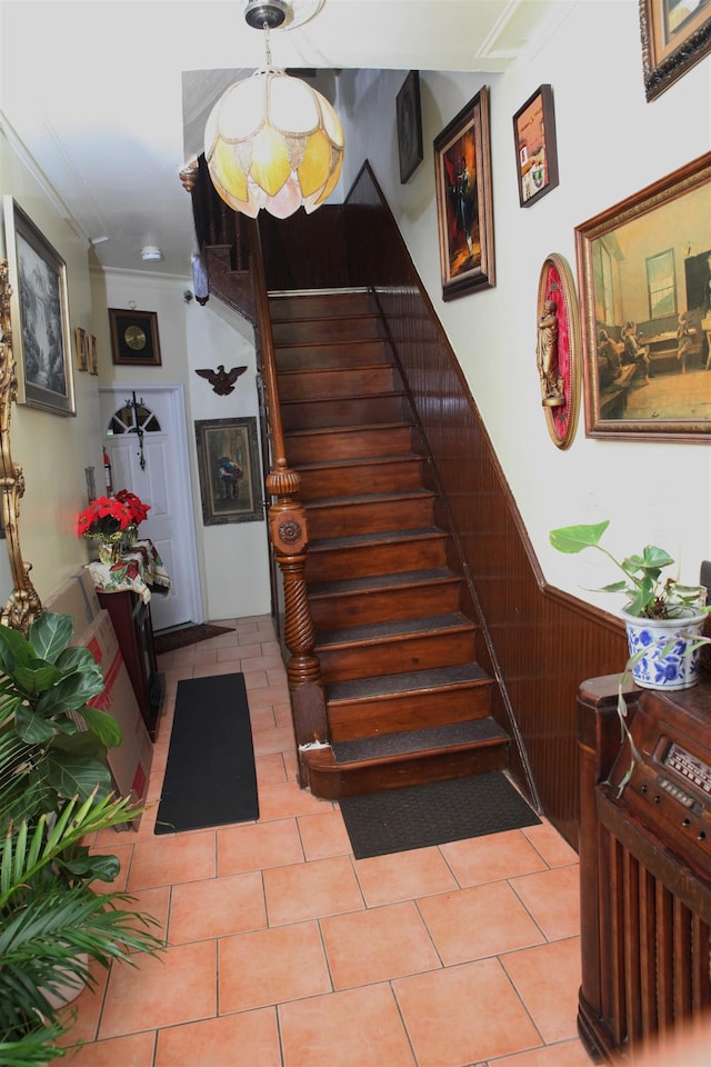 stairs with tile patterned flooring, a wainscoted wall, and ornamental molding