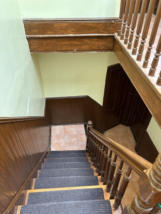 stairs with tile patterned floors, wooden walls, and wainscoting