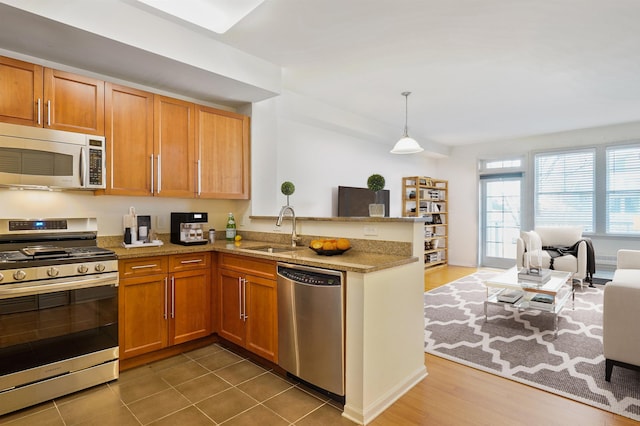 kitchen featuring appliances with stainless steel finishes, a sink, open floor plan, a peninsula, and light stone countertops
