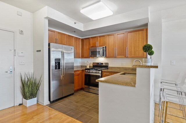 kitchen featuring appliances with stainless steel finishes, a sink, brown cabinetry, and dark tile patterned flooring