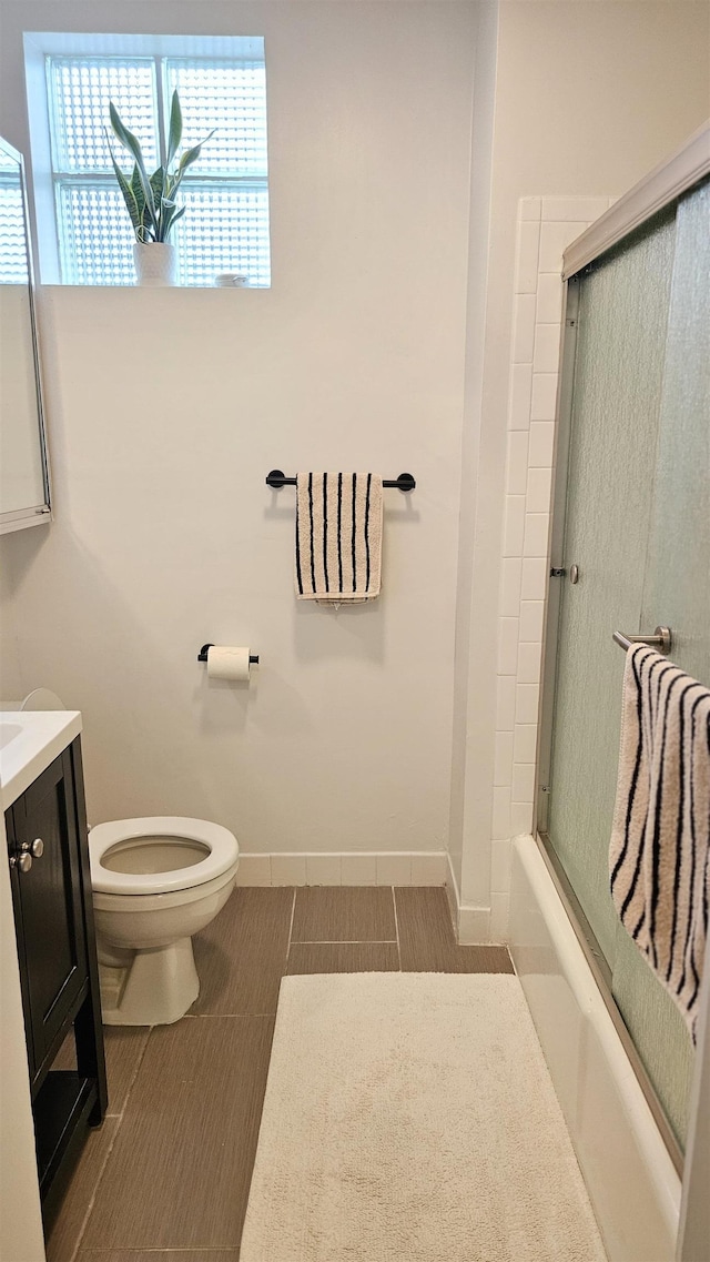 full bath featuring toilet, baseboards, enclosed tub / shower combo, and vanity