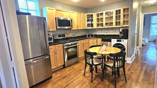 kitchen featuring backsplash, washer / clothes dryer, dark countertops, stainless steel appliances, and dark wood-type flooring
