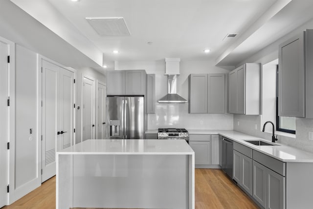 kitchen featuring stainless steel appliances, gray cabinetry, a sink, a center island, and light wood finished floors