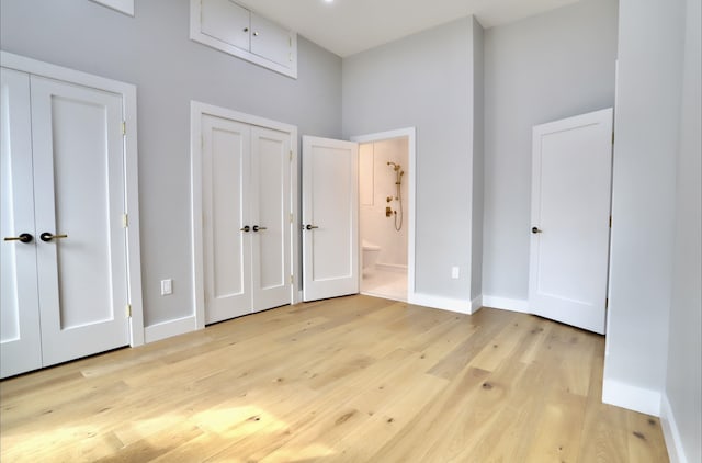 unfurnished bedroom with connected bathroom, two closets, and light hardwood / wood-style flooring