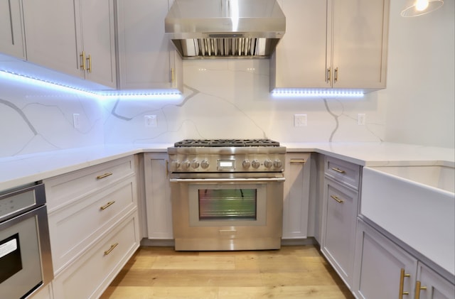 kitchen with tasteful backsplash, high end stainless steel range oven, light stone counters, light hardwood / wood-style floors, and wall chimney range hood