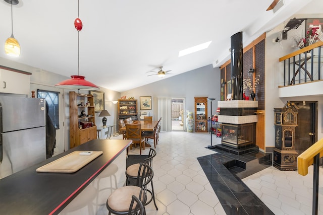 kitchen featuring tile patterned floors, decorative light fixtures, stainless steel refrigerator, ceiling fan, and vaulted ceiling with skylight