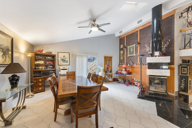 tiled dining space with ceiling fan and vaulted ceiling with skylight