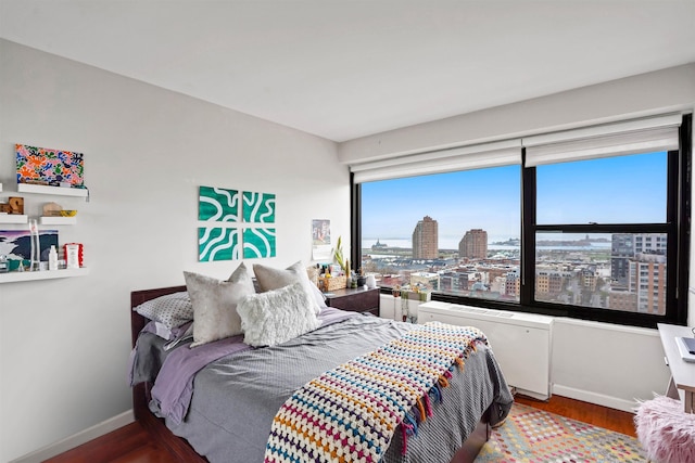 bedroom with a view of city, baseboards, and wood finished floors