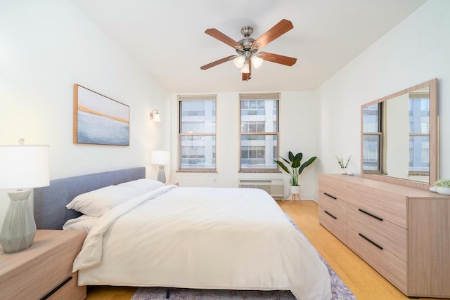 bedroom featuring light wood-type flooring, ceiling fan, and a wall unit AC