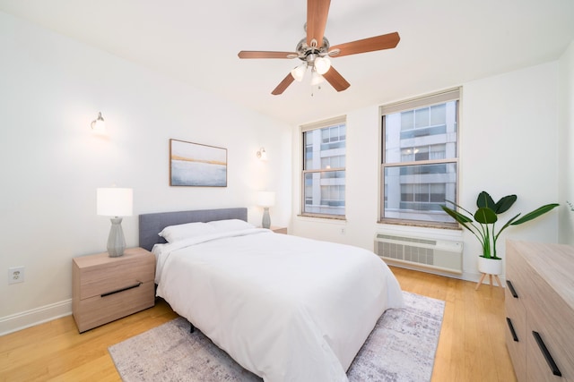 bedroom with a ceiling fan, an AC wall unit, baseboards, and light wood finished floors