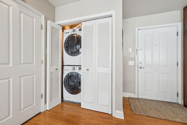 clothes washing area featuring baseboards, laundry area, stacked washer / dryer, and light wood-style floors