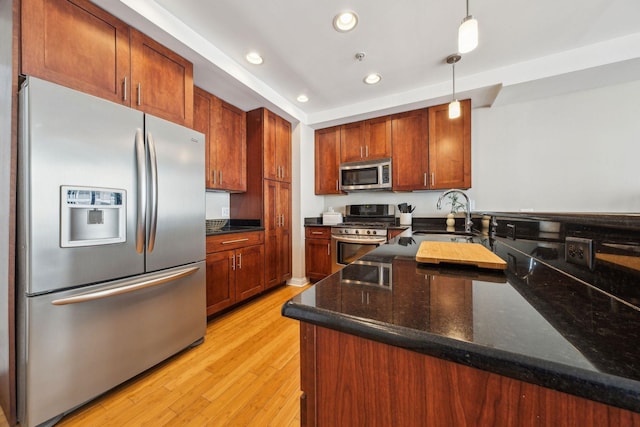 kitchen featuring hanging light fixtures, appliances with stainless steel finishes, dark stone counters, a sink, and light wood-type flooring