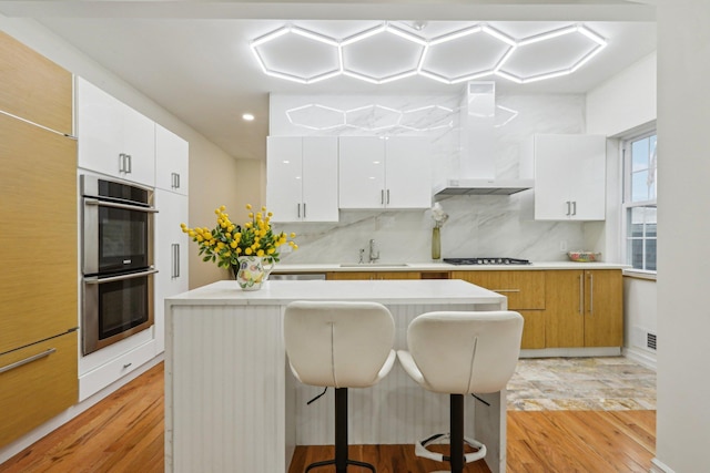 kitchen with double oven, light wood-type flooring, a center island, a breakfast bar area, and recessed lighting