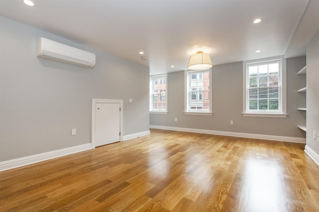 interior space featuring baseboards, recessed lighting, an AC wall unit, and light wood-style floors