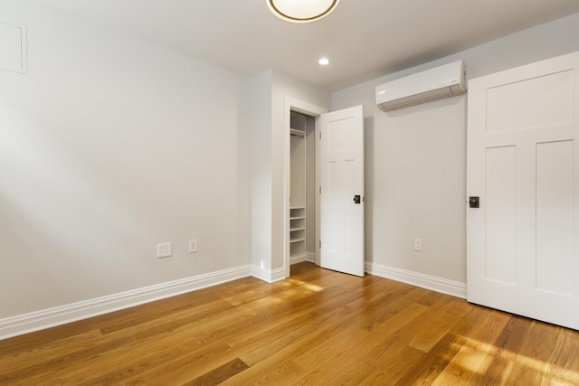 unfurnished bedroom with recessed lighting, a wall mounted air conditioner, light wood-type flooring, and baseboards