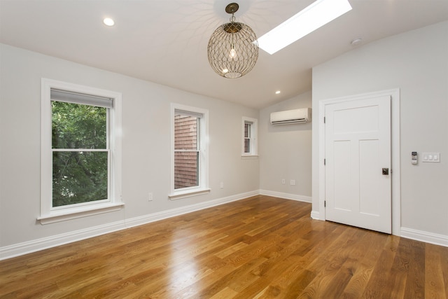 unfurnished room featuring baseboards, a wall unit AC, recessed lighting, vaulted ceiling with skylight, and wood finished floors