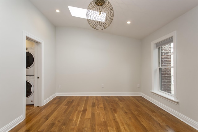 spare room featuring wood finished floors, a skylight, baseboards, and stacked washer and dryer