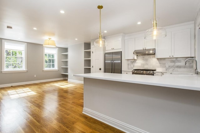 kitchen featuring under cabinet range hood, light countertops, appliances with stainless steel finishes, a peninsula, and a sink