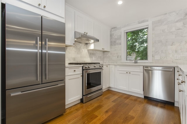 kitchen featuring high quality appliances, under cabinet range hood, a sink, white cabinetry, and light countertops