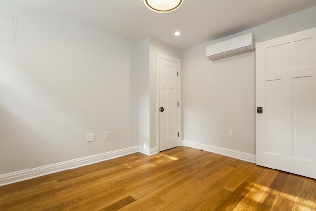 unfurnished bedroom featuring recessed lighting, a wall mounted air conditioner, light wood-style floors, and baseboards