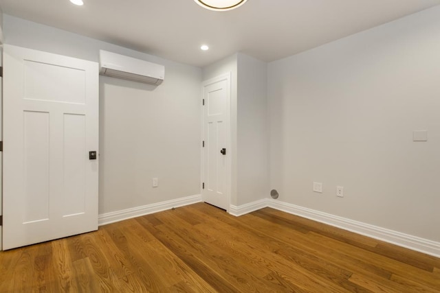 interior space with a wall unit AC, recessed lighting, wood finished floors, and baseboards